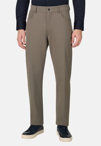 Pantalon beige taille slim à la texture lisse, avec deux poches avant et une fermeture à bouton, assorti à des baskets foncées.