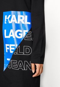 Czarna odzież z długim rękawem z niebieską prostokątną grafiką z pogrubionym białym tekstem "KARL LAGERFELD JEANS" i gładką teksturą.
