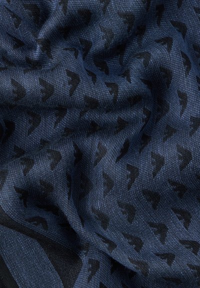 Modrá tkanina s textúrovaným vzorom malých čiernych uhlových tvarov, zobrazená v jemných záhyboch zdôrazňujúcich jej tkanie a dizajn.