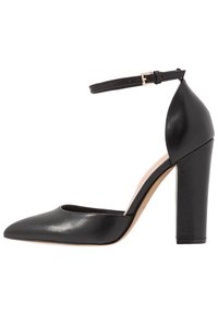 Černá kožená lodička na vysokém podpatku s špičatou špičkou, kotníkovým páskem a silným blokovým podpatkem. Hladká textura s minimem ozdob.