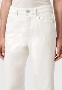 Jeans in denim bianco con vita alta, design a cinque tasche e hardware in bottone argentato. Presentano un tessuto testurizzato e una gamba dritta.