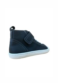 Zapato alto de cuero negro con costuras blancas, correa de Velcro y suela de goma. Cuenta con una asa en la parte posterior para facilitar su uso.