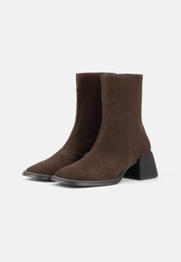 Brown suede ankle boots with a smooth texture, pointed toe, and a chunky black heel. Zipper closure on the inner side for easy wear.