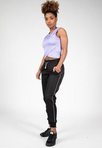 Zwarte joggingsbroeken met witte zijstrepen, voorzien van een elastische tailleband en boorden, gecombineerd met een lavendelkleurige mouwloze top.