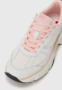 Weißer Sneaker mit rosa Akzenten, aus Mesh- und Leder-Materialien, runder Form, dicker Sohle und "LOVE MOSCHINO" Text auf der Zunge.
