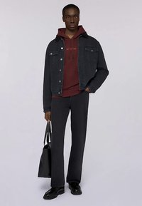 Czarna kurtka dżinsowa na bordowym kapturze, w połączeniu z ciemnymi rozszerzanymi spodniami i czarnymi butami. Trzyma czarną torbę na ramię.