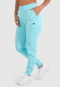 Lichtblauwe joggingbroek met witte zijpiping, elastische tailleband en zakken. Gekocht met witte sportschoenen. Soepele, casual stoftextuur.