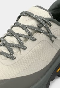 Chaussure de randonnée gris clair avec tige texturée, lacets gris à pois blancs, et semelle extérieure en caoutchouc foncé. Détails Vibram sur la semelle.