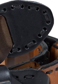 Black leather strap with brown accents, featuring decorative stitching and a rounded end. The texture appears smooth and durable.