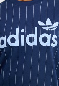 Navy blue cotton t-shirt with vertical white stripes, featuring a light blue "adidas" logo and a trefoil emblem on the chest.
