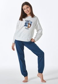 Weißer Pullover mit blauer und brauner Druckschrift; kombiniert mit navyblauen Jogginghosen mit elastischen Bündchen. Lässige, bequeme Passform.