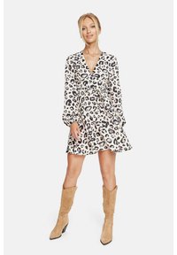 Vestido envolvente de color claro con estampado de leopardo negro, mangas largas y cintura ceñida, combinado con botas de rodilla de color beige.