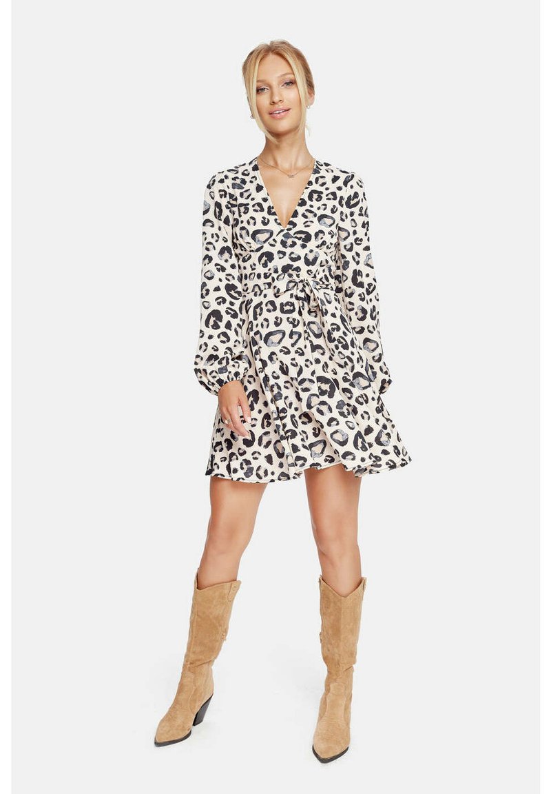 Vestido envolvente de color claro con estampado de leopardo negro, mangas largas y cintura ceñida, combinado con botas de rodilla de color beige.