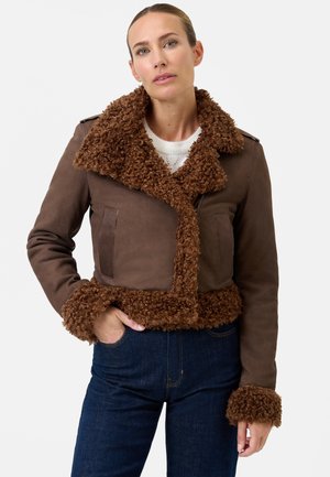 Brun cropped jakke med en plysset, krøllet brun pelskrave og -manchetter, der har en glat ydre overflade og to forlommer.
