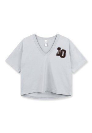 T-shirt gris clair court avec col en V, manches courtes, et un chiffre '10' brodé en brun foncé sur la poitrine gauche. Matière douce en coton.