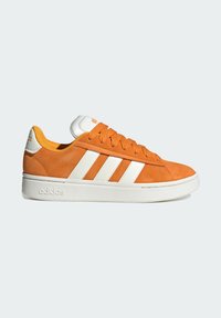 Zapatillas de ante naranja con tres rayas blancas de Adidas, suela blanca, cordones y talón blanco, mostradas de lado sobre un fondo claro.