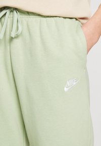 Pantalones de chándal verde claro fabricados con un tejido suave, con cintura elástica y cordón. Presentan un logo de Nike en blanco bordado en la pierna.