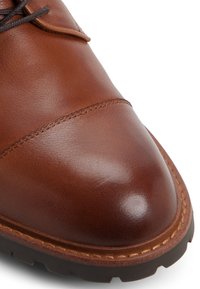 Zapato de cuero marrón con un acabado suave, punta redondeada y suela de goma oscura en contraste. Presenta un detalle de costura sutil a lo largo del borde.