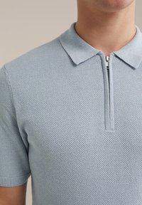 Tricou polo albastru deschis, realizat dintr-un material texturat, având un închidere cu fermoar scurt, mâneci scurte și un guler clasic.