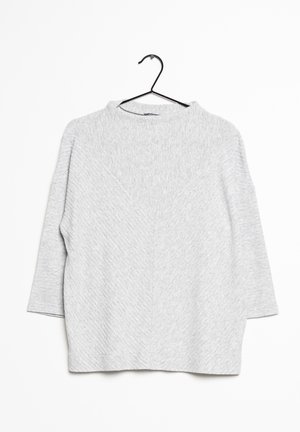 Pull en tricot gris clair texturé à manches trois quarts suspendu sur un cintre noir sur fond blanc.