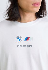 Hvid bomulds t-shirt med BMW og M logoer i grå og farvede striber, med ordet "Motorsport" trykt nedenfor i en fed skrifttype.