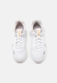 Ζευγάρι λευκά αθλητικά παπούτσια Nike με μπεζ λογότυπα Swoosh, υφασματικό πλέγμα και κορδόνια,  σε θέα από πάνω σε απλό φόντο.