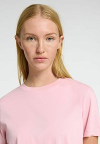 Camiseta de algodón rosa claro con cuello redondo y mangas cortas, con una textura suave y sin patrones ni acentos visibles.