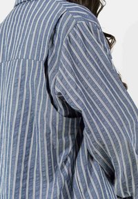 Blauw gestreept shirt van gestructureerde stof, met verticale witte strepen en een ontspannen pasvorm. Zichtbare rugpas en licht ingevette mouwen.