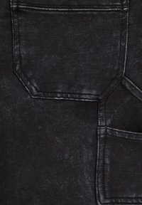 Čierna tkanina s textúrovaným povrchom, dvoma vreckami na nášivkách, jemným opotrebovaním a kontrastným prešívaním po okrajoch.