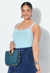 Ljusblå tanktopp med spetsdetaljer och rhinestones, matchad med en jeanskjol. Håller en turkos vävd handväska med fransdetaljer.
