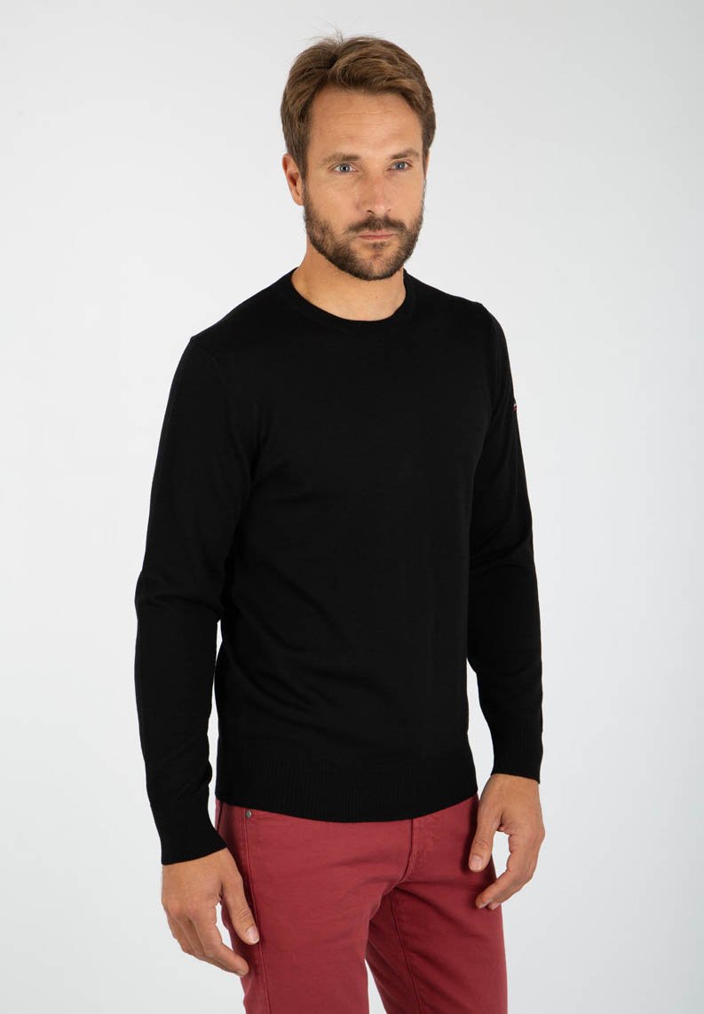 Sort langærmet sweater med rund hals, ribbet kant og en glat tekstur. Bæret med røde bukser, har den et lille logo på ærmet.