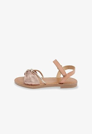 Sandalias rosas con un detalle en la punta metálico brillante, suela plana, correa ajustable en el tobillo y un intrincado diseño de nudo en la parte superior.