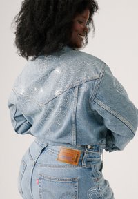 Veste en denim avec un détail en rhinestones complexe en motif tourbillon à l'arrière. Tissu en denim bleu, coupe classique, associée à un jean taille haute.