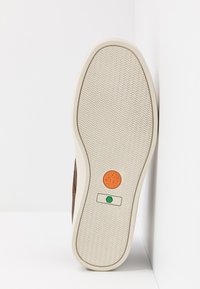 Bruine schoenzool met golvende textuur, voorzien van een oranje en groene logo en accenten. De rand is crèmekleurig met een patroon in de loop.