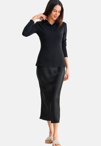 Zwarte geribbelde longsleeve polo gecombineerd met een stijlvolle zwarte satijnen midi rok. Platte, lichtgekleurde sandalen maken de outfit compleet.