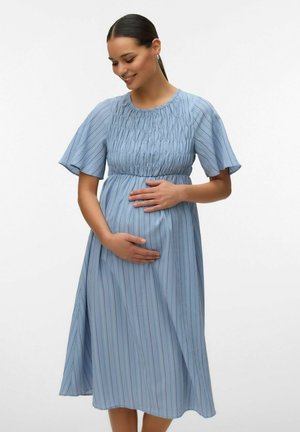 Rase rase naeratab, kandes sinist triibulist põlvpikkust kleiti, hoides õrnalt mõlema käega kõhtu.