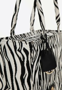 Canvas draagtas met een zwart-wit zebrapatroon, voorzien van stevige handvatten en een kleine zwarte leren accent met een metalen ring.