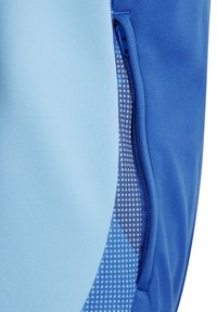 Blauw sportkledingstuk met een ritszak. De stof heeft een gladde textuur met een contrasterende mesh voering met een netwerkpatroon.