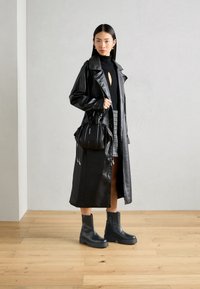 Svart lær trench coat med innsvingt midje, kombinert med en svart genser med høy hals, rutete mini skjørt og svarte ankelstøvler.