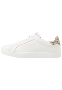 Vit lågtopp sneaker med snörning fram, beige hältab med svarta logotyper och präglad branding på sulan.