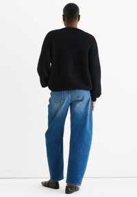 Black knitted sweater with loose fit, paired with light blue high-waisted jeans. Black flat shoes complete the outfit.
