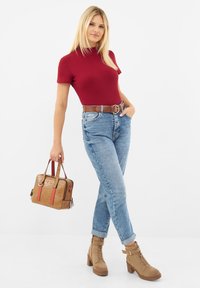 Haut rouge ajusté à manches courtes, jean taille haute bleu clair, ceinture marron, bottines à talons beiges, et un sac en bandoulière texturé beige avec des accents rouges.