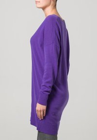 Fialový svetřík s dlouhým rukávem a volným střihem, se žebrovanými manžetami a lemem. Měkká textura se slabým splýváním, sahající do poloviny stehen.