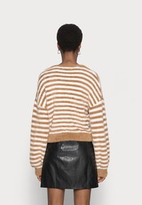 Gestreifter Pullover in Braun und Weiß, aus flauschigem Material gefertigt. Hat lange Ärmel und eine cropped Länge, kombiniert mit einem schwarzen Lederrock.