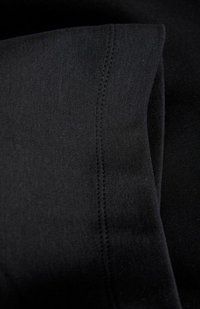 Schwarzer Stoff mit einer glatten Textur, der eine sichtbare Naht und eine gefaltete Kante aufweist. Das Material wirkt weich und dehnbar.