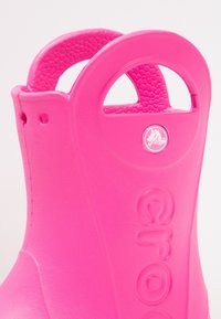 Sabot en caoutchouc rose avec surface texturée et poignées en forme de découpe circulaire. Inclut le logo de la marque et un texte de logo en relief sur le côté.