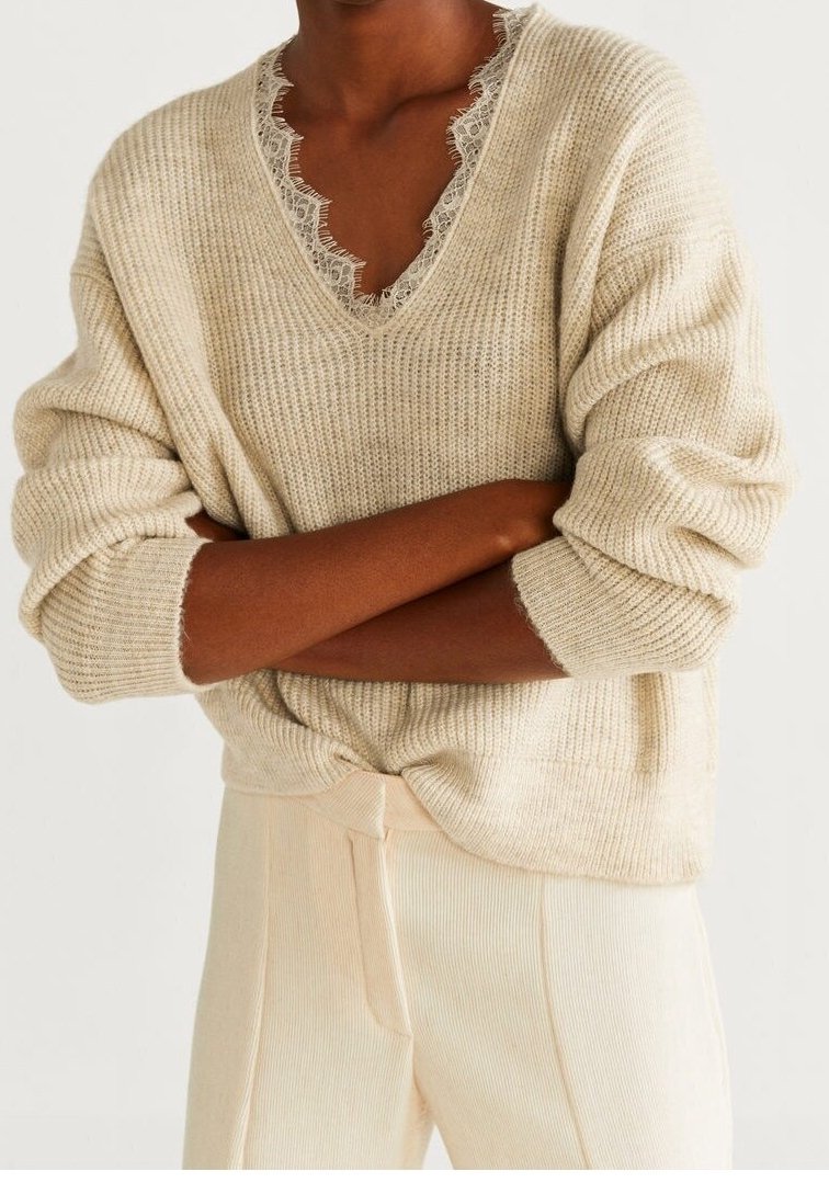 Personne portant un pull côtelé couleur crème avec un col en V bordé de dentelle et un pantalon côtelé assorti taille haute, les bras croisés.