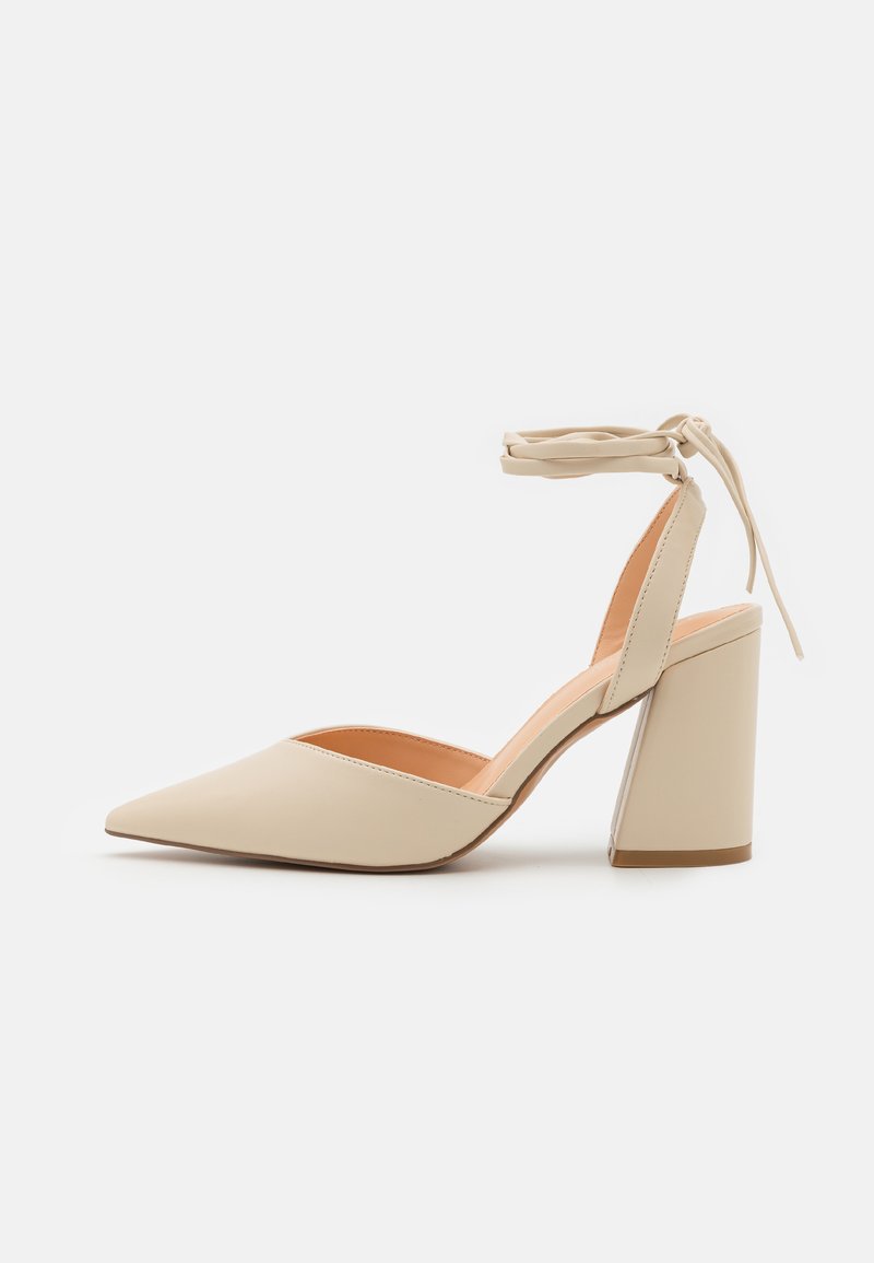 Beige høye hæler med spiss tå, ankelstropp og bred blokkheel. Glatt syntetisk materiale med matt finish.