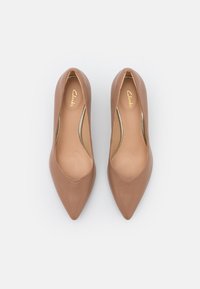 Paire de ballerines en cuir taupe à bout pointu pour femmes avec semelles intérieures beiges estampillées "Clarks" présentée sur fond blanc.