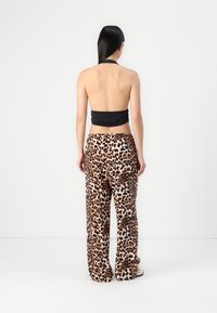 Haut dos nu noir associé à un pantalon large à imprimé léopard, présentant un motif texturé dans des nuances de marron et de crème. Vue de dos montrée.